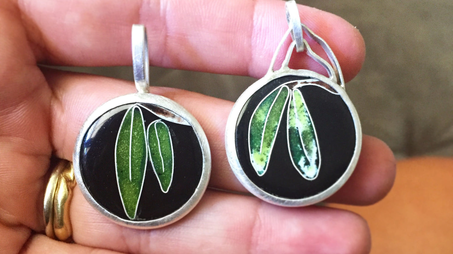 Pair of earrings with green leaf design held in a hand.