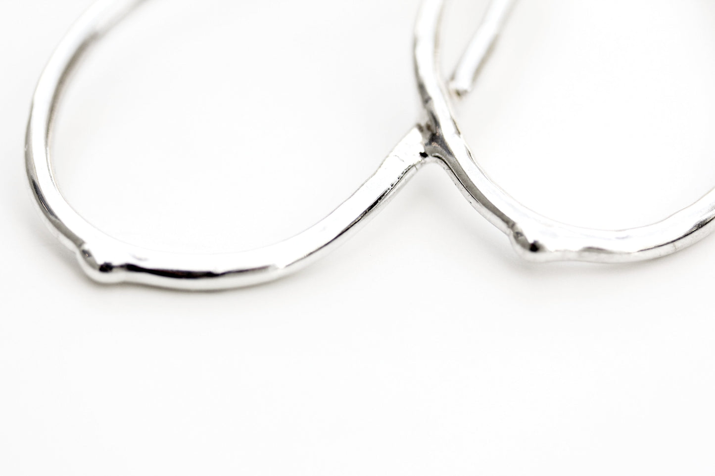 Detail photo of a pair of silver earrings with an organic vine-like texture.