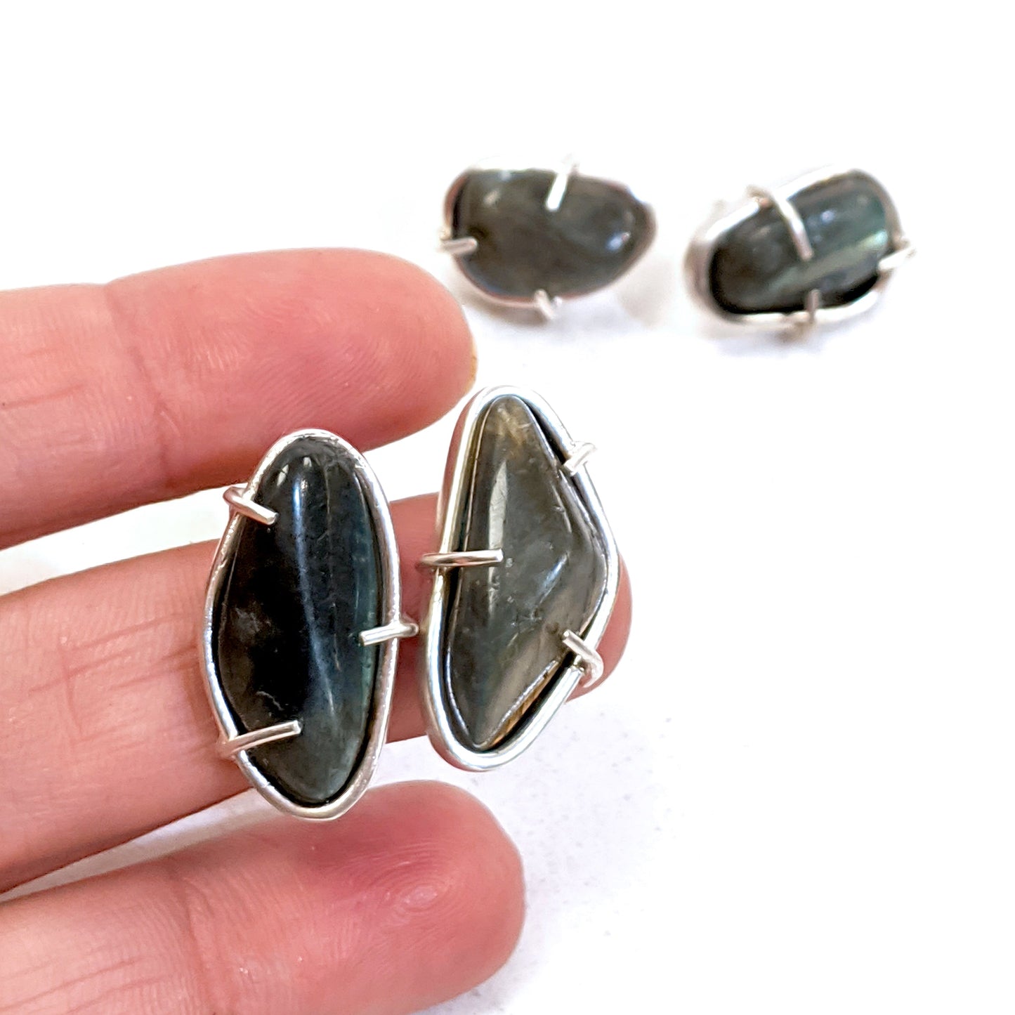 Full view of Cassius Studs with hand in background to help give an idea of its scale. Irregularly shaped and smoothly tumbled Labrodorite stones are set simply in Sterling Silver.