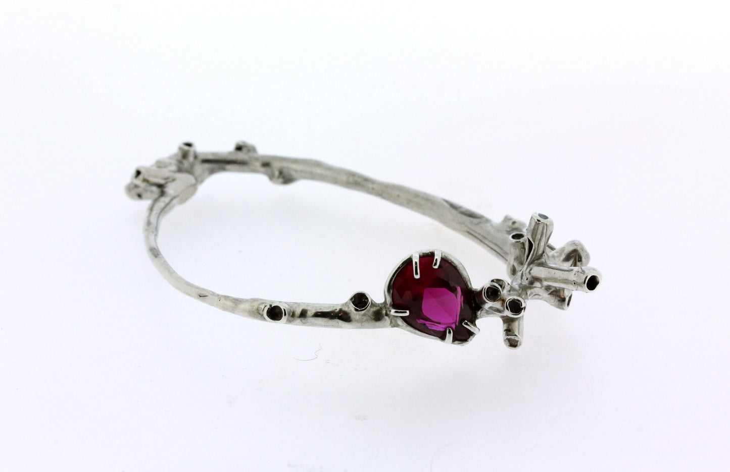 Close up view of Camari bangle. Organic, sculptural tube like features wrap the wrist in an irregular shaped bangle. A Lab Grown Ruby is perched amongst clusters of sea-sponge like details.