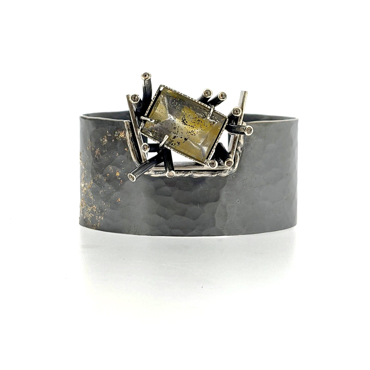 Full frontal view of Malissa bracelet. This stunning cuff bracelet is fabricated in Sterling Silver with an asymmetric cluster of Champagne Diamond studded tubular elements surrounding a stunning, one of a kind gold-fleck dappled Mirror quartz. A splattering of 14K gold balances the design, a continuation of the golden flecks that are a characteristic of this unique central stone.