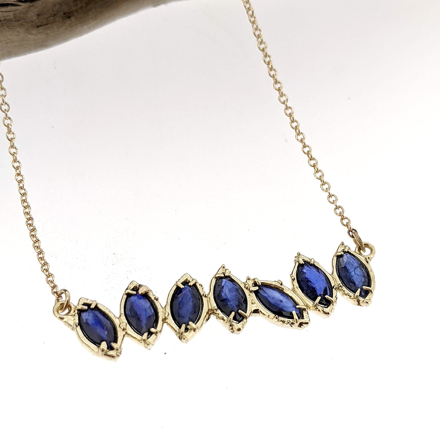 Close up view of pendant on Sapphire Cherin Necklace. Seven Sparkling natural marquise shaped Blue Sapphire stones delicately adorn this irregular line-style bar necklace with subtle organic detailing.