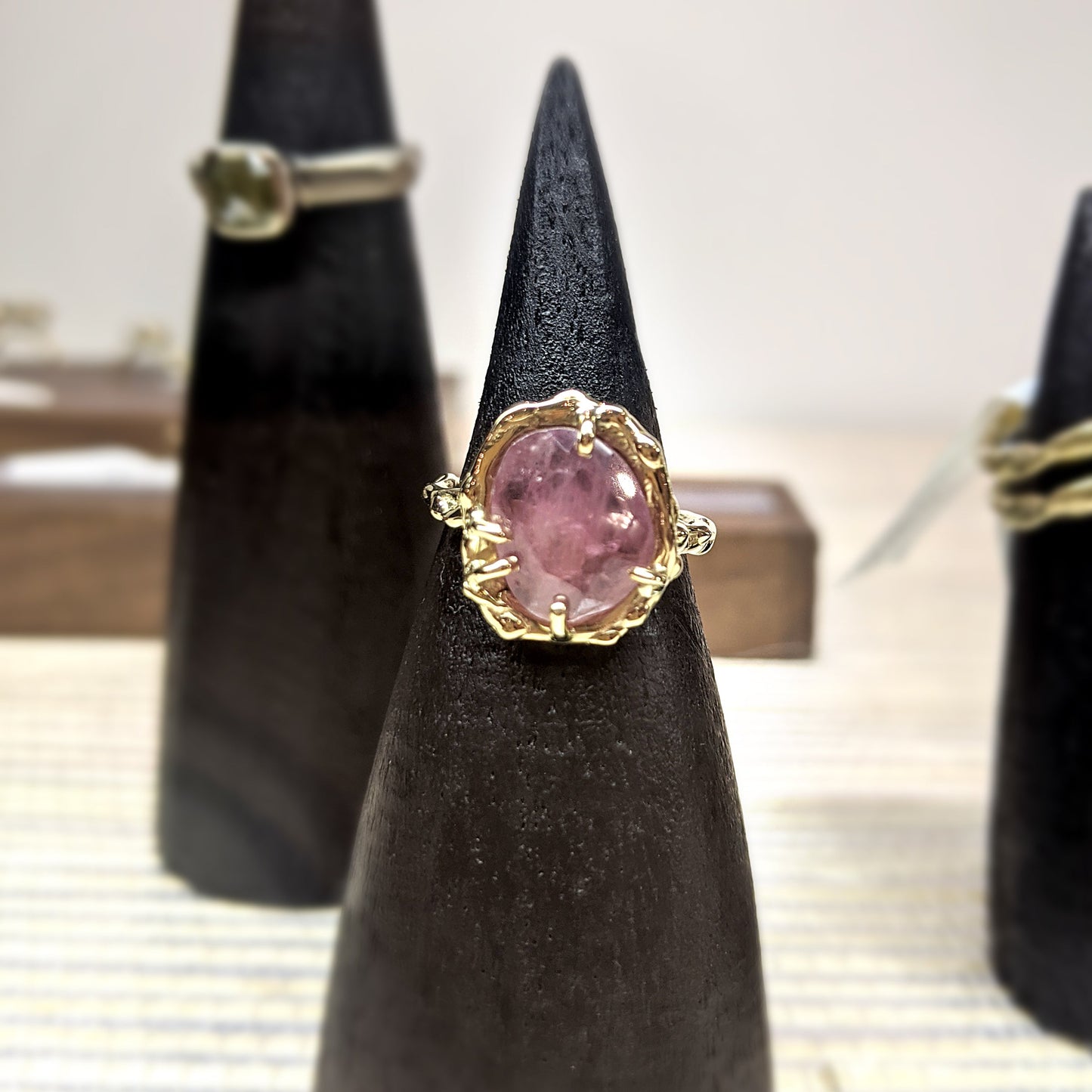 Full view of Roxanna Ring - Large on black pedestal. The Roxanna features organic carved metalwork with a delicately dappled surface. A large 1.4 asymmetrical shaped Umba Sapphire in a beautiful shade of pale pink is set in 14K (recycled) Yellow Gold.