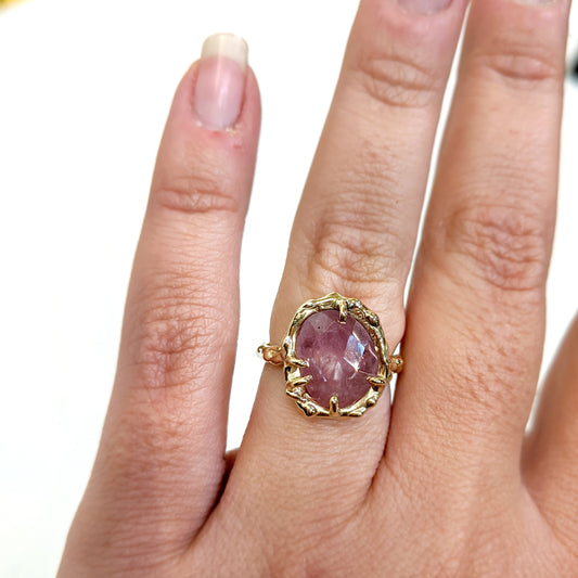 Full view of Roxanna Ring - Large on a woman's hand to help give an idea of its scale. The Roxanna features organic carved metalwork with a delicately dappled surface. A large 1.4 asymmetrical shaped Umba Sapphire in a beautiful shade of pale pink is set in 14K (recycled) Yellow Gold.