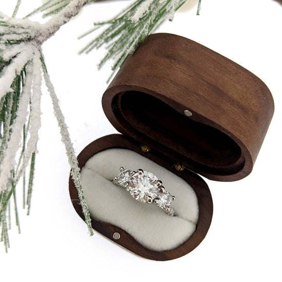 Wooden ring box with a diamond ring inside, set against a snowy branch background