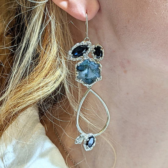 Close-up of a person wearing a silver earring with blue gemstones.