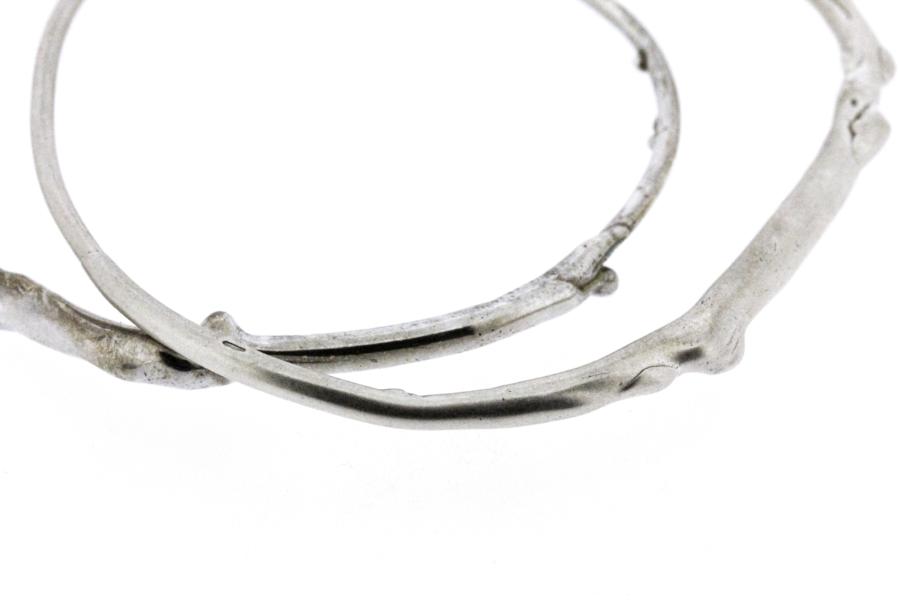 A detail photo of two sterling silver bangle bracelets that have a smooth organic texture that looks as if they are twigs covered in ice.