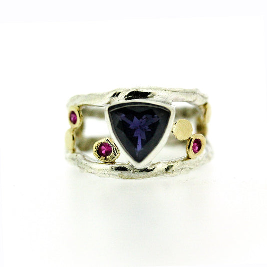 Full view of Esme Ring. This wide band beauty celebrates negative space and color.  Her center stone is a bright, royal Iolite that is an intense shade of deep purple.  Surrounding her are a scattering of Natural Pink Sapphires and 14K Yellow gold accent dots.  She's capped by two Sterling Silver Bands.