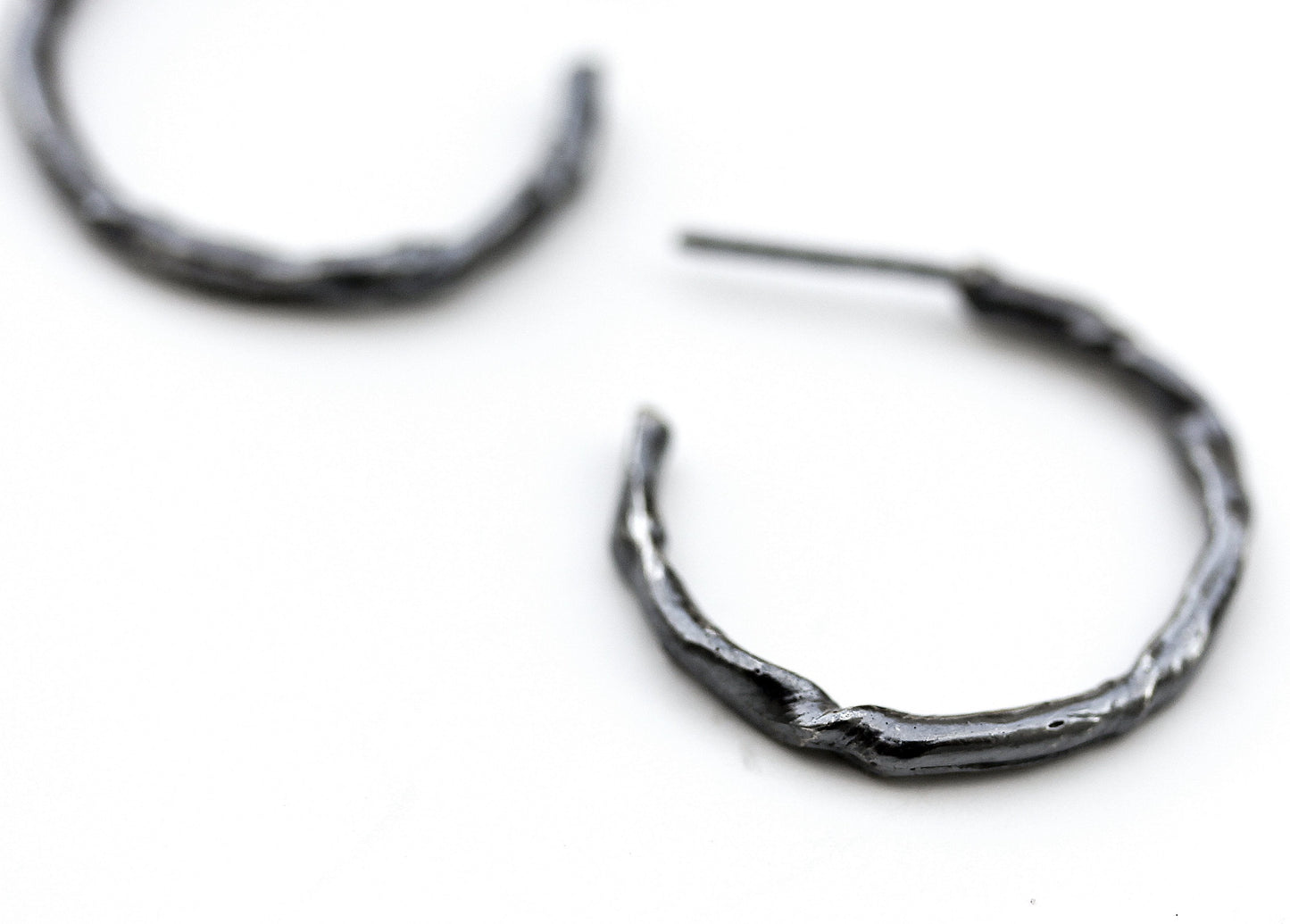 Detail photo of a blackened silver hoop earring with an organic vine-like texture.