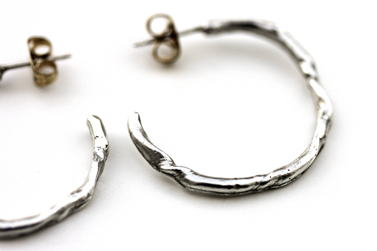 Detail photo of a silver hoop earring with an organic vine-like texture.