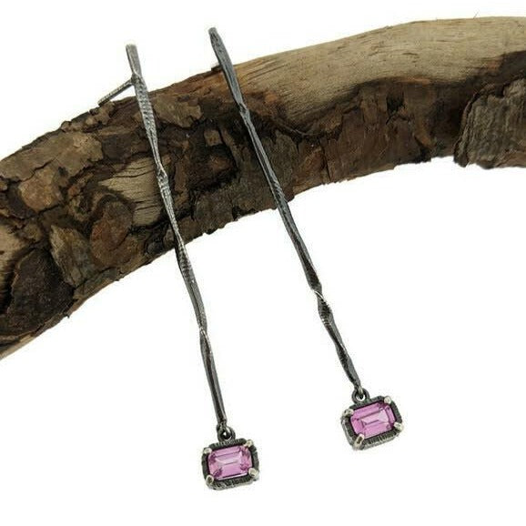 Full view of Pink Sapphire Gina Dangle Earrings laying on top of a stick. A contemporary, organic twist on a simple stick earring featuring a dangling emerald cut Pink Sapphire.