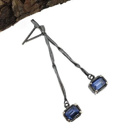 Full view of Blue Sapphire Gina Dangle Earrings. A contemporary, organic twist on a simple stick earring featuring a dangling emerald cut Blue Sapphire.