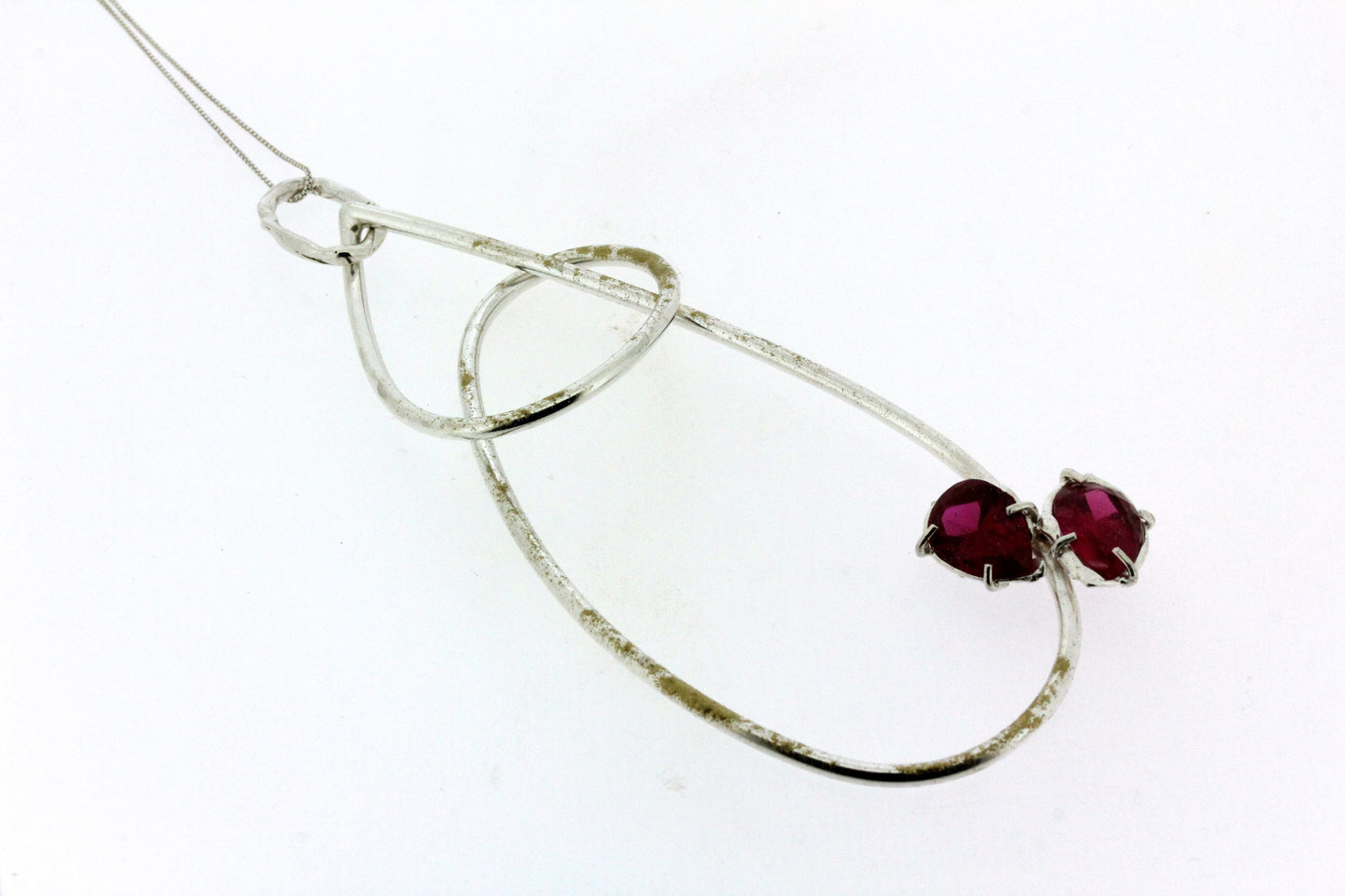 Close up view of pendant on Cindy Necklace. This large pendant is made of silver wire and resembles the shape of a wrapped teardrop with two set ruby's on the right side, there are also accents of gold powdercoat throughout the pendant.