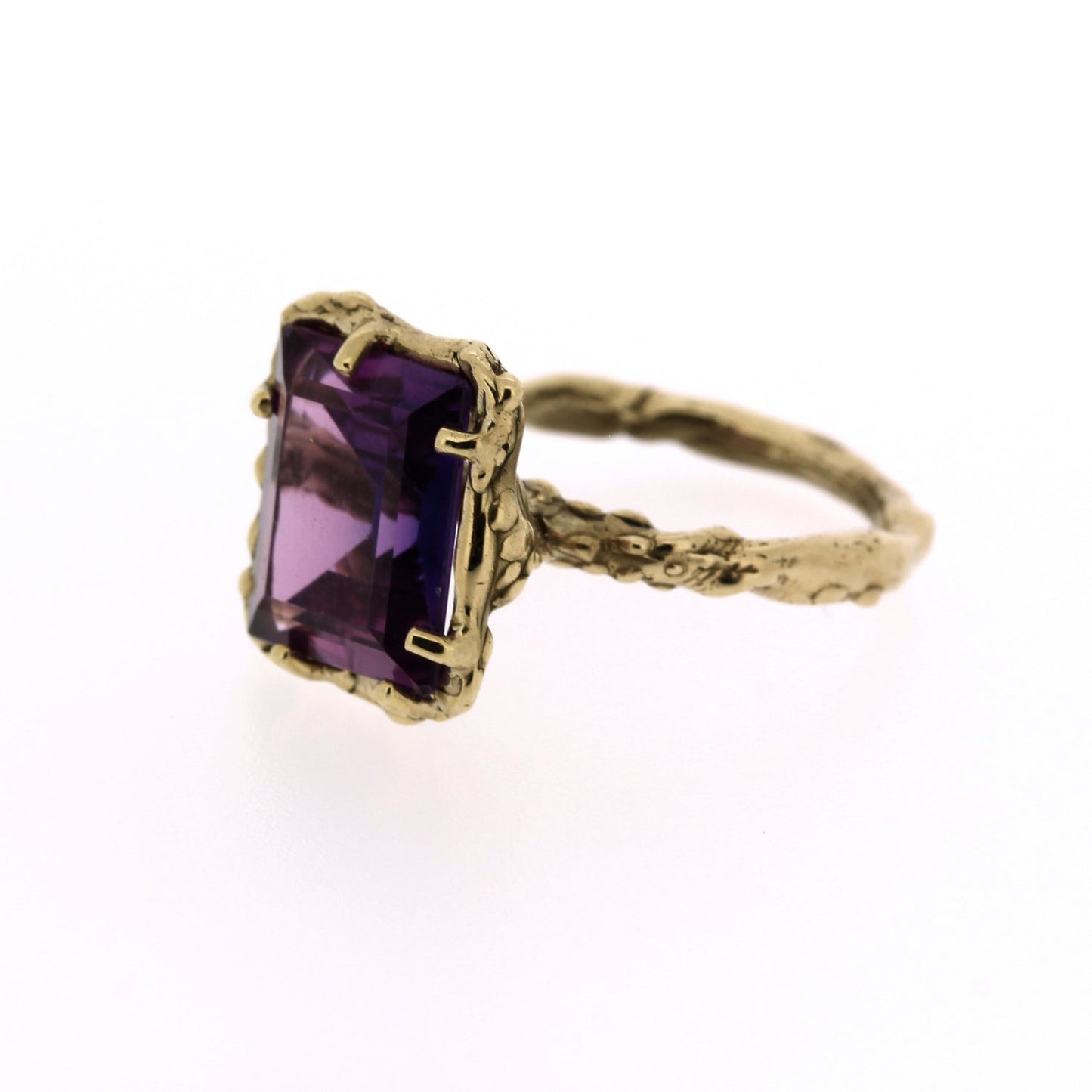 Full view of side of Giovanna Ring. This ring is made of yellow gold, ahs an organic texture throughout its setting and band and has a set rectangular purple sapphire at the top.