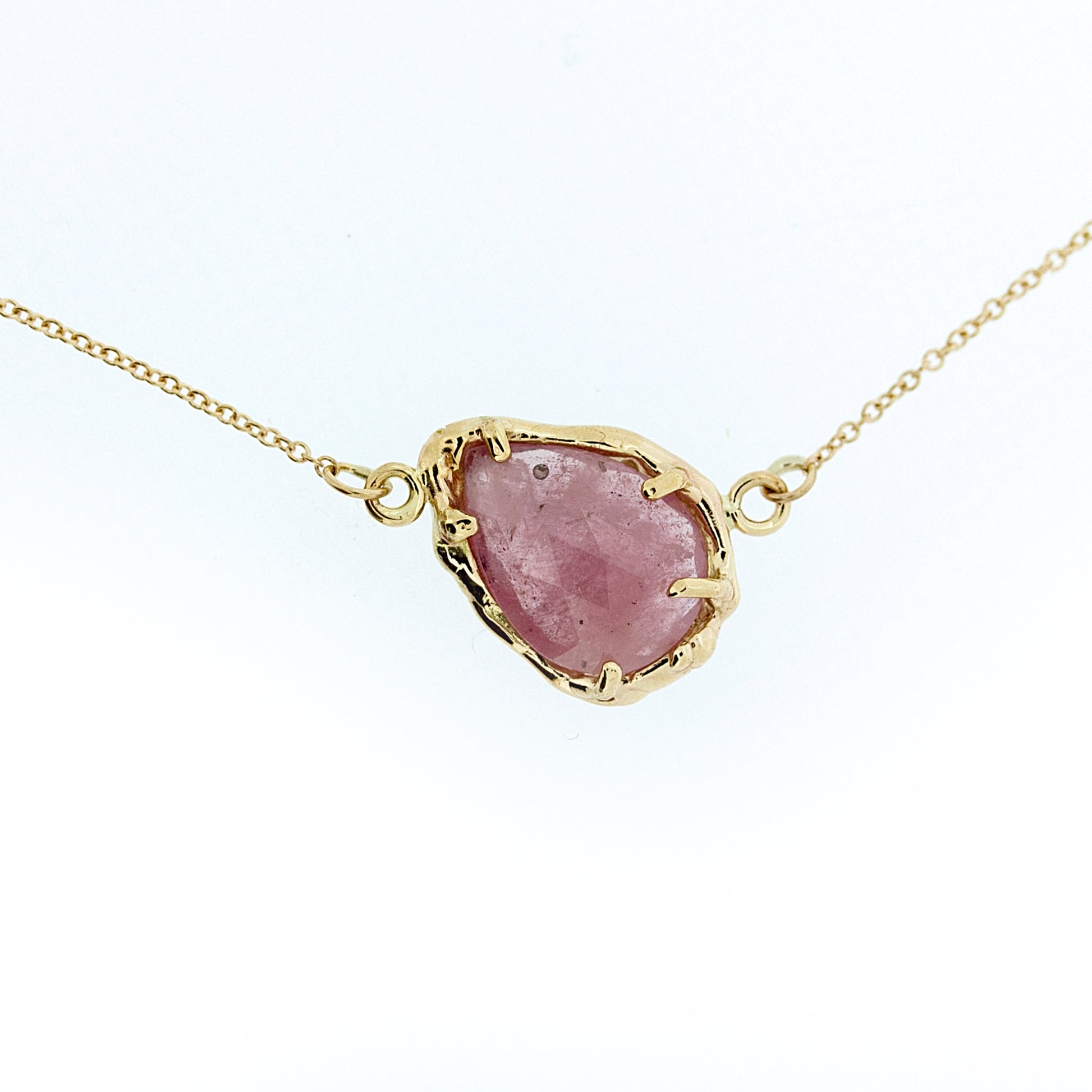 Close up of pendant on Marta necklace. A lovely imperfect rose cut Umba Sapphire perched at an angle along it's chain in a subtle peachy pink tone.  This gemstone is surrounded by organic, highly textured 14K Yellow Gold. On a dainty 16" solid 14K yellow gold chain.