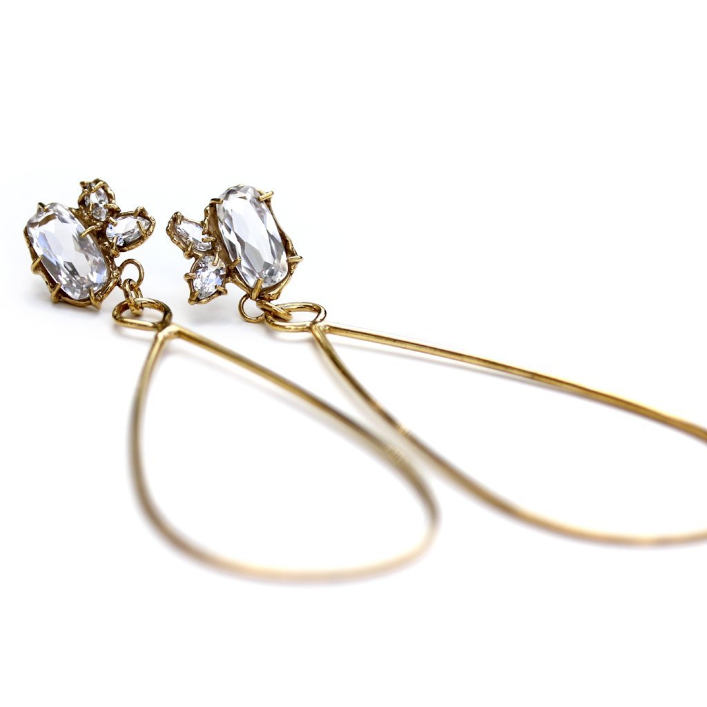 Long, gold statement earrings with a cluster of white topaz gemstones at the top and a tear drop shaped dangle.
