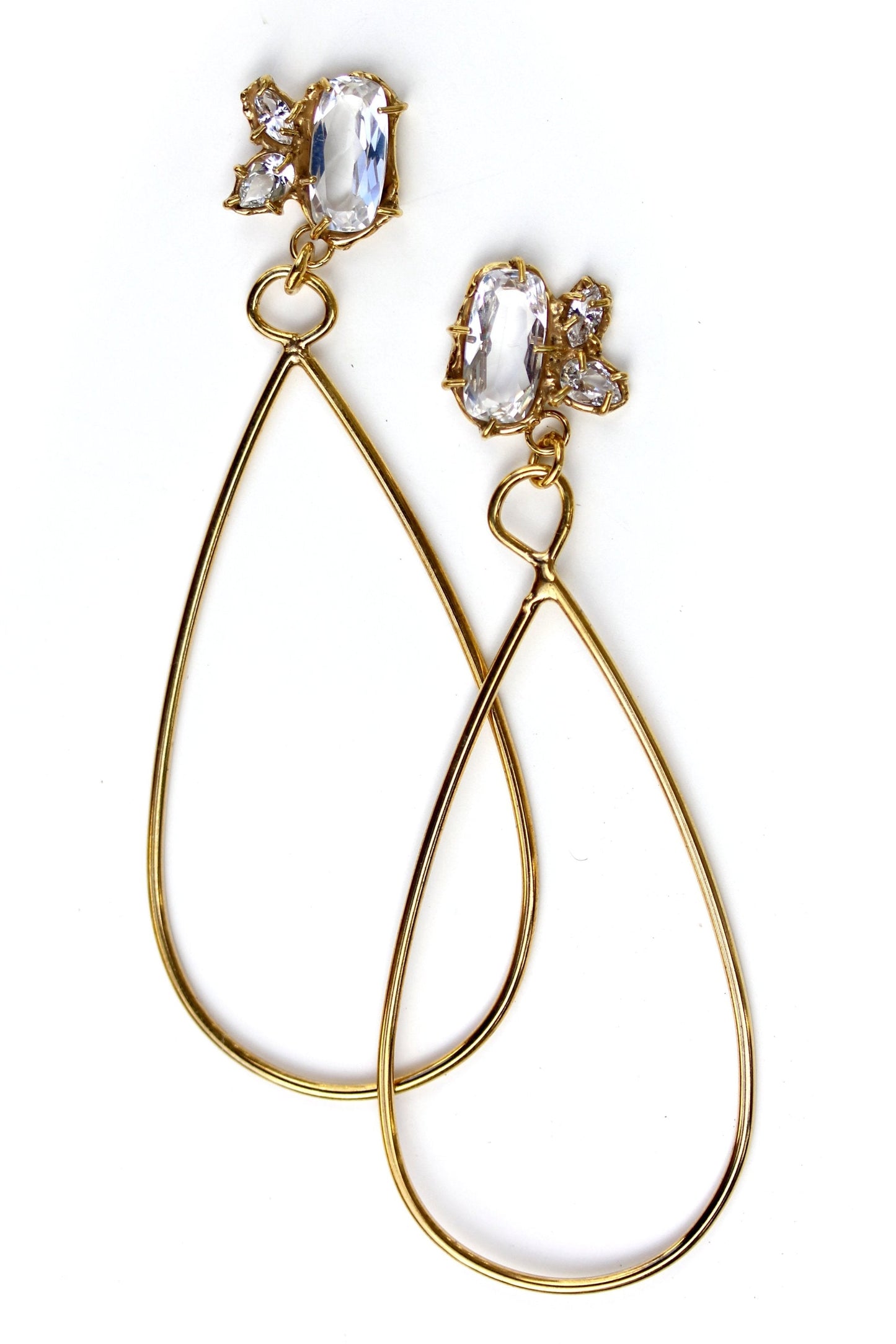 Long, gold statement earrings with a cluster of white topaz gemstone in various shapes at the top and a tear drop shaped dangle.
