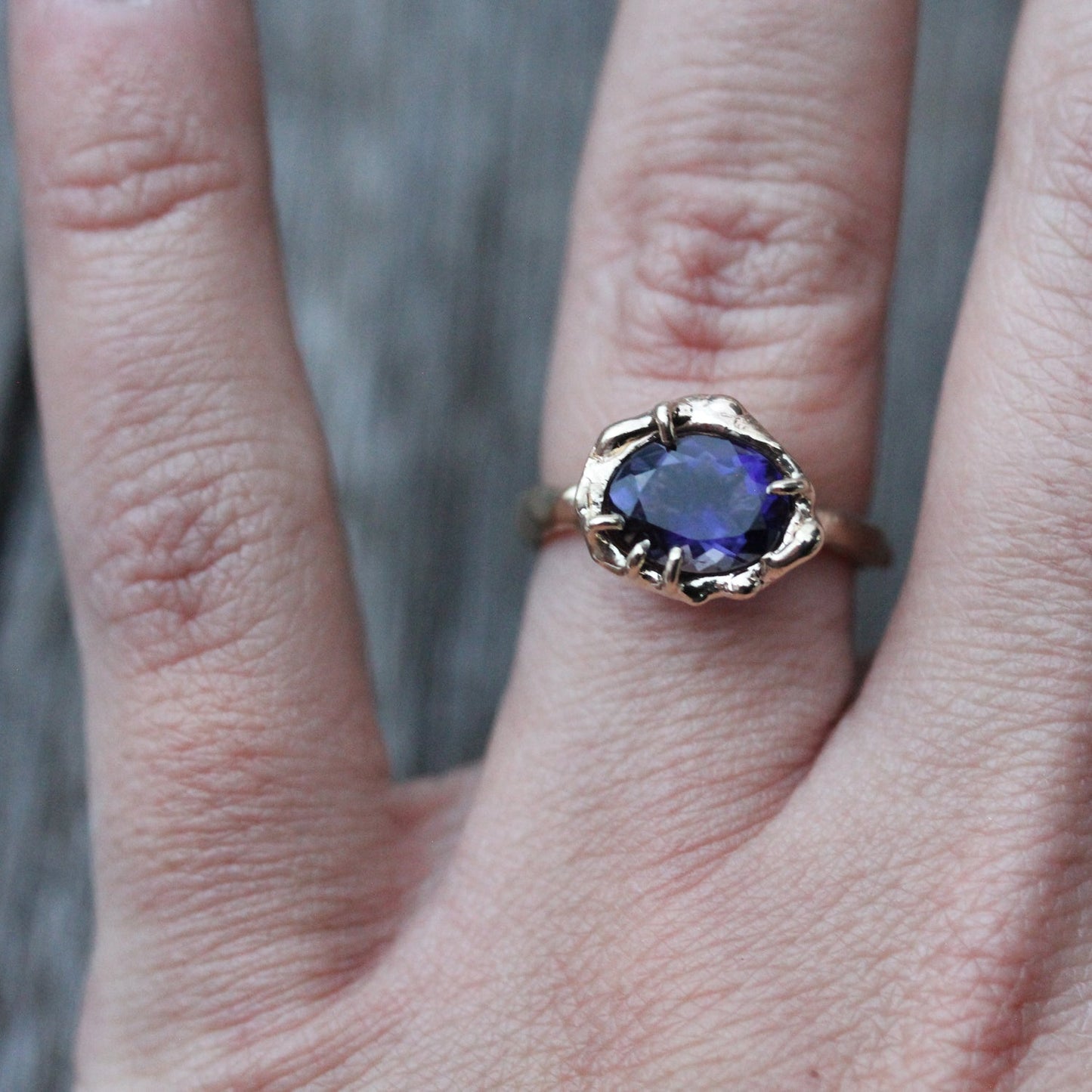 Full view of Nada Ring on woman's hand to help give an idea of its scale. This beautiful purple stone is set in a one of a kind organic hand wrought setting.  Her beautiful curves and vibrant color are a perfect match.  Set in 14K Yellow gold to complement her outstanding, almost glowing color.  