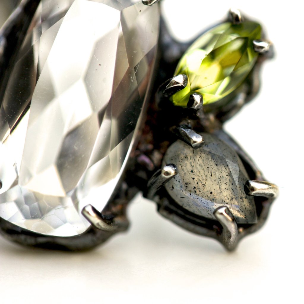 Detail photo of an earring with white topaz, peridot and labradorite prong set in blackened sterling silver.