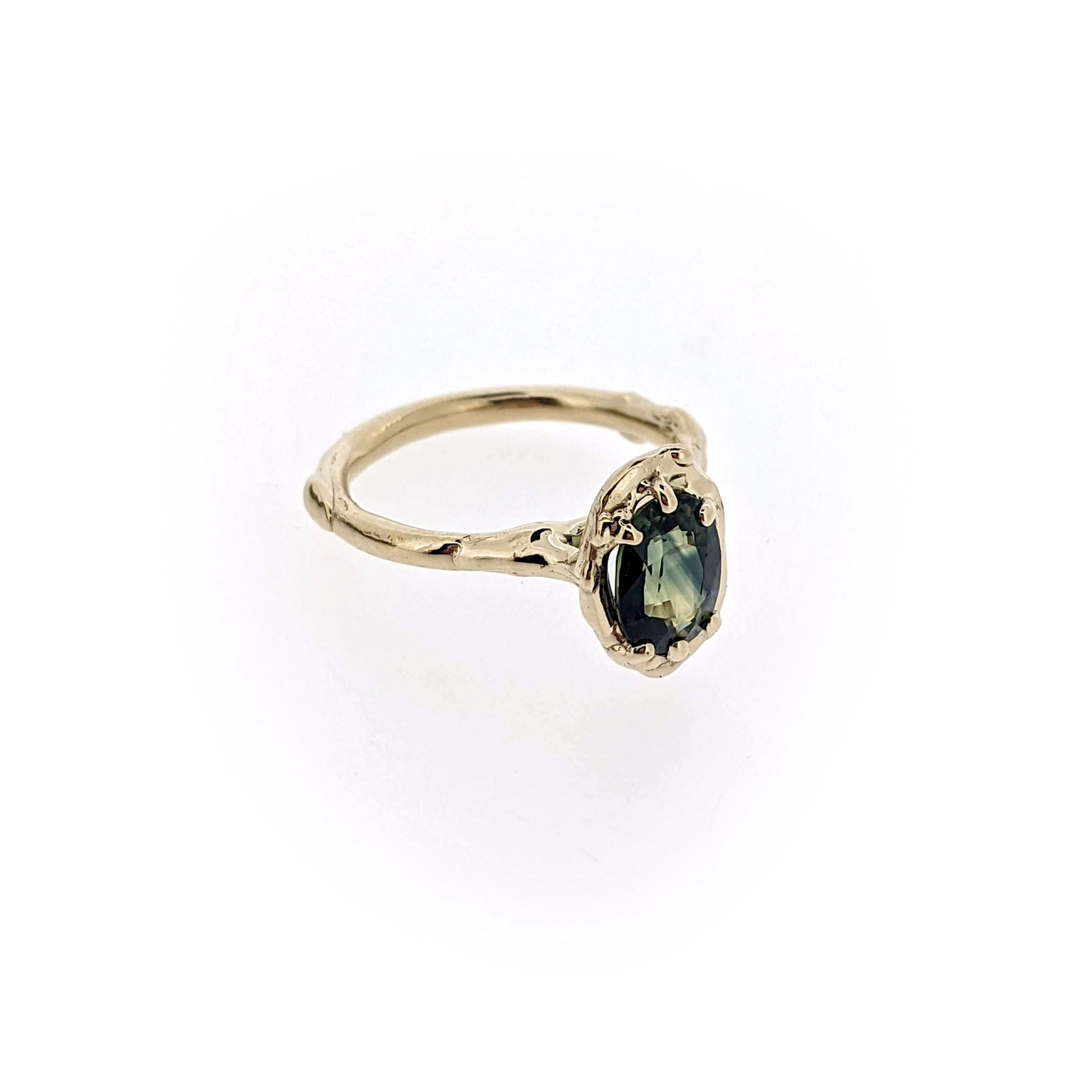 Angled view of Rianna Ring. Rianna features a sweet 1.65 Carat VVS multi-color Sapphire from Austrailia is nestled in an organic recycled 14K yellow gold setting.  This sapphire is stunning -- and reflects a blend of blues, greens, and yellows depending on how the light passes through.  
