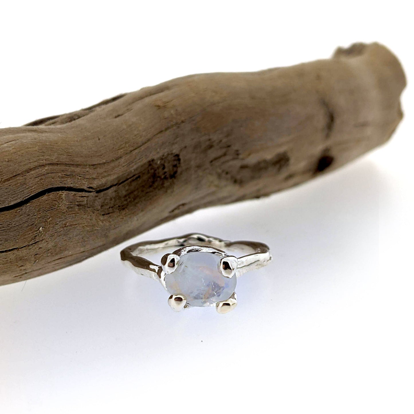 organic design rainbow moonstone and sterling silver solitaire ring, shown displayed next to driftwood.