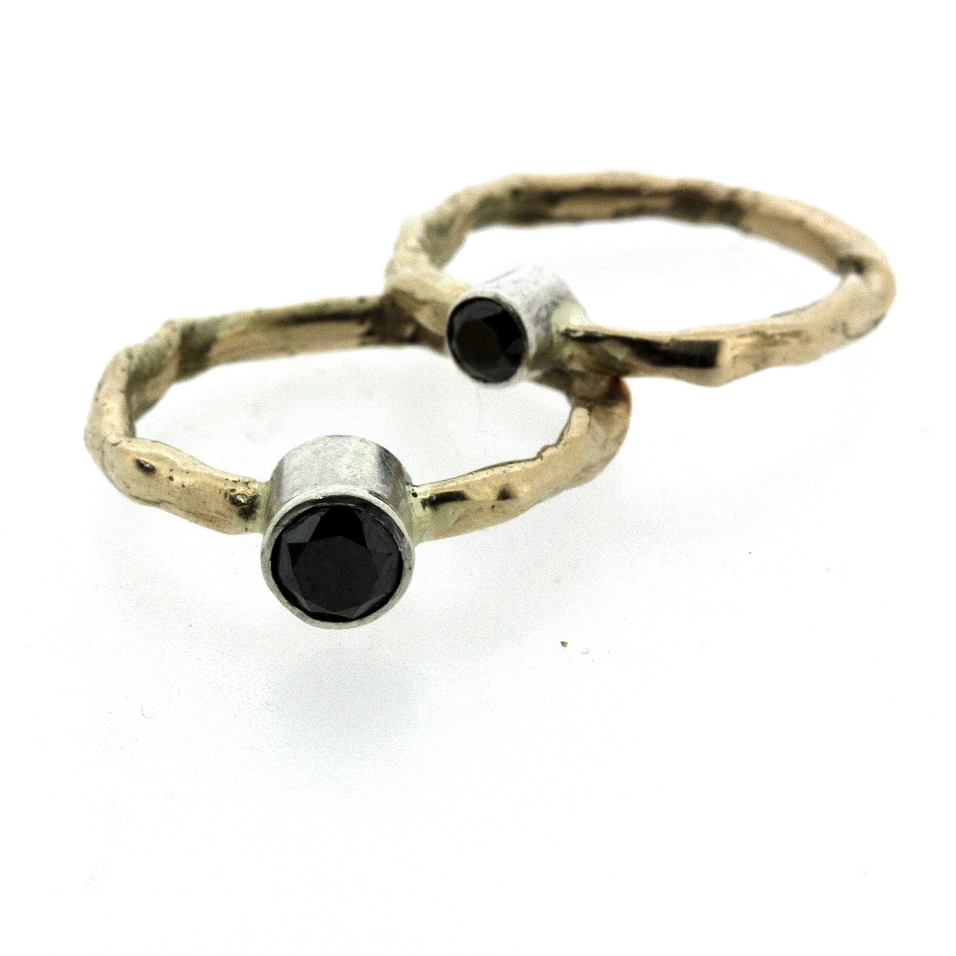 Full view of two Rita Rings stacked on top of one another. These rings have an organic gold band, a black diamond and a silver bezel surrounding the black diamond.