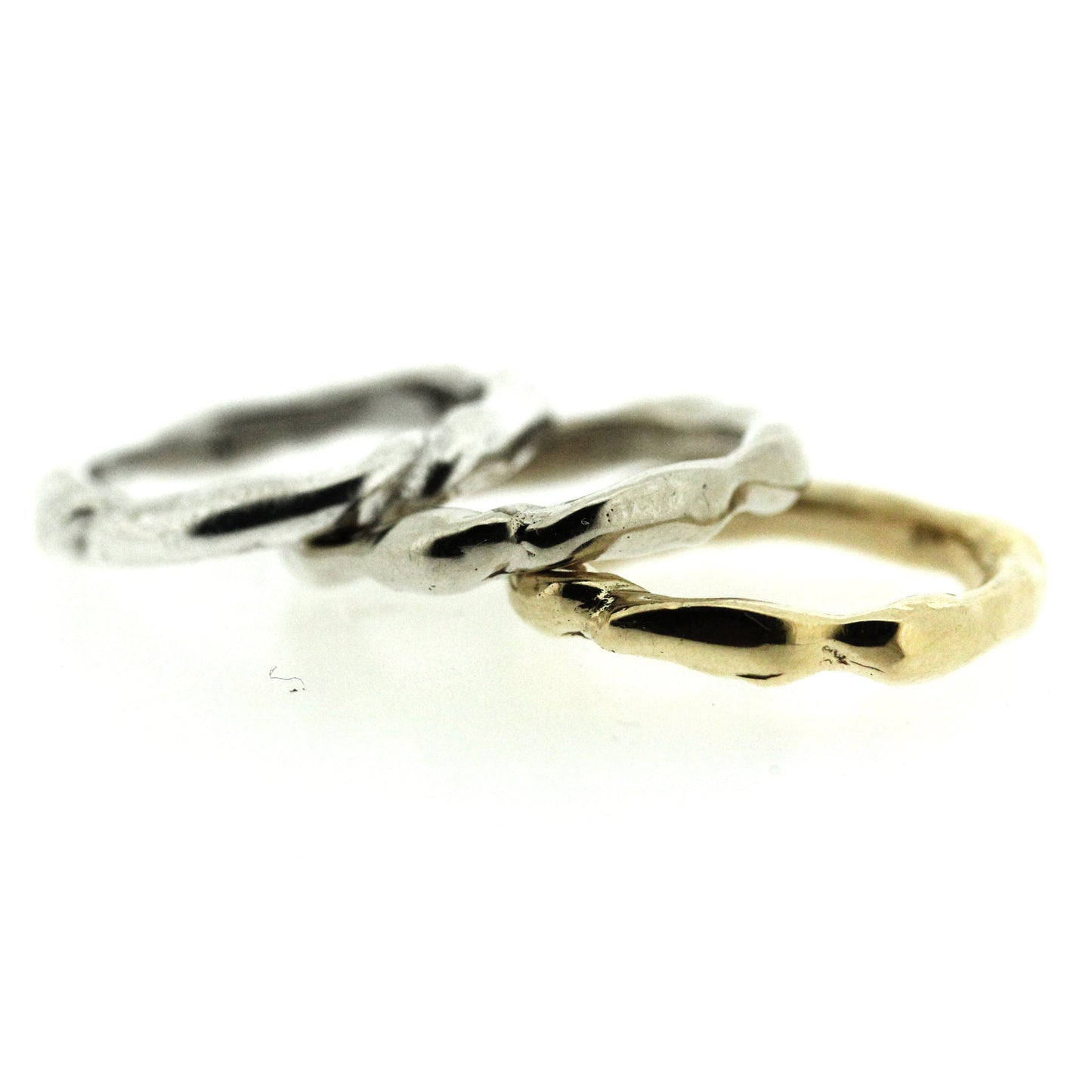 Full view of silver, white gold, and yellow gold Surge Bands stacked on top of one another.