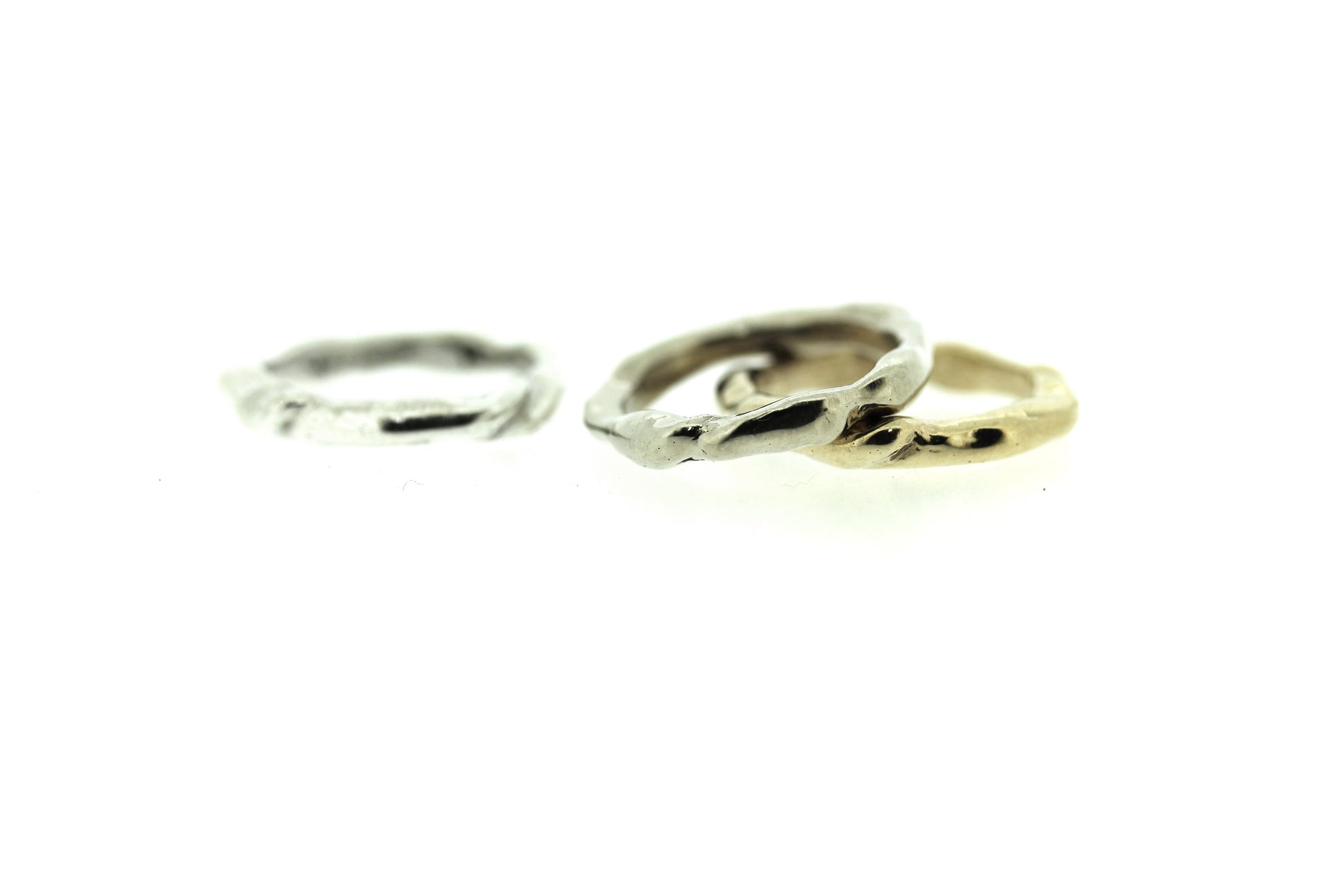 Full view of silver and gold Surge Band stacked on top of one another and white gold band standing off to the side.