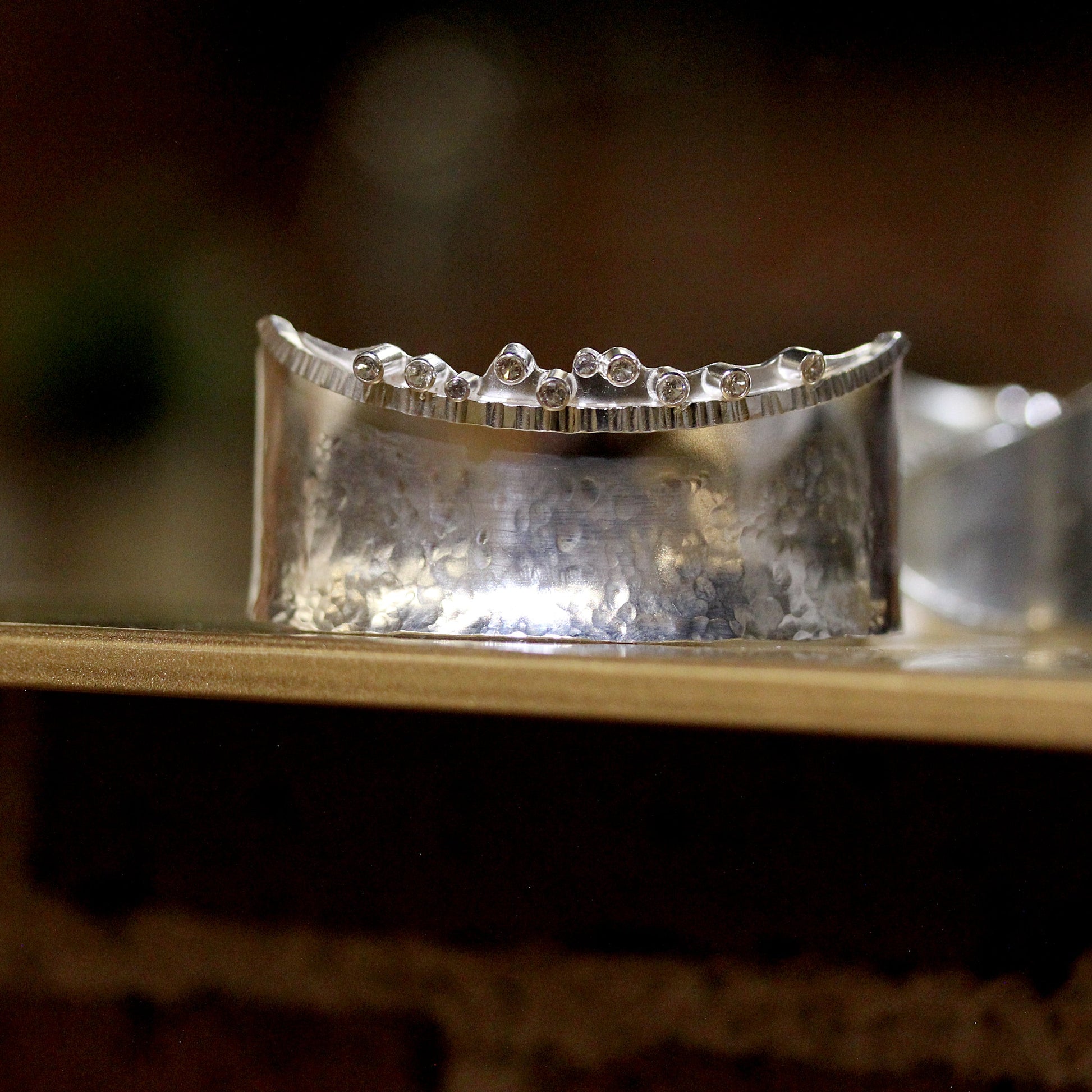 Top view of Angelina Cuff. This cuff is made of silver and has a hammered texture throughout and ten set white sapphires at the top of one side.