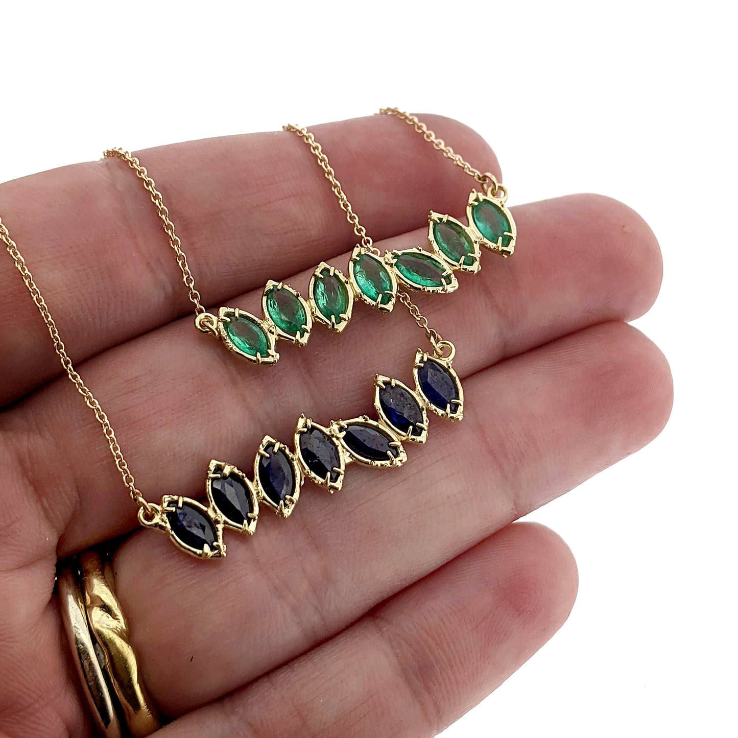 Full view of green and blue Cherin Necklaces hanging from woman's hand to help give an idea of their scale.
