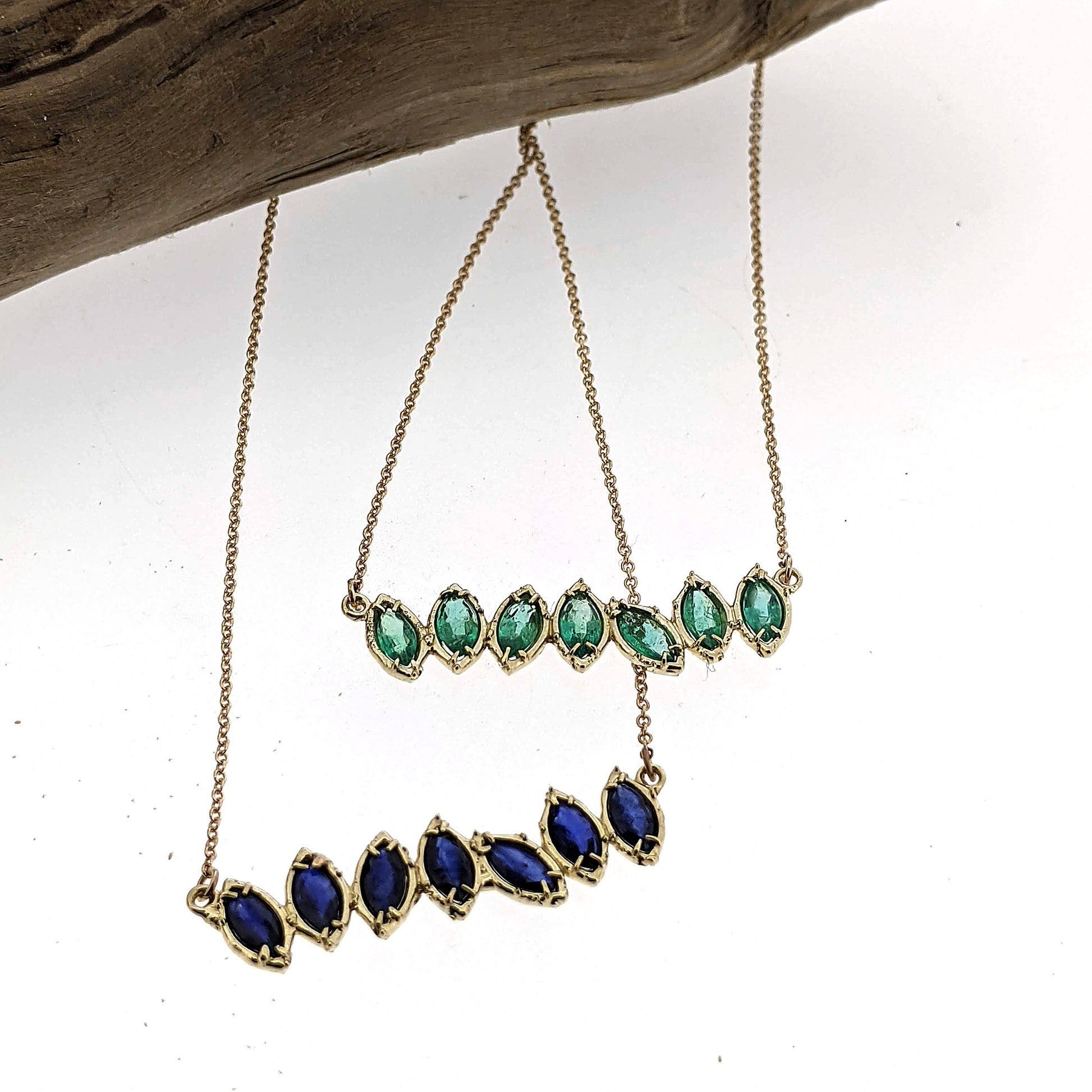 Close up view of pendants on sapphire blue and peridot Cherin Necklace with stick in background.