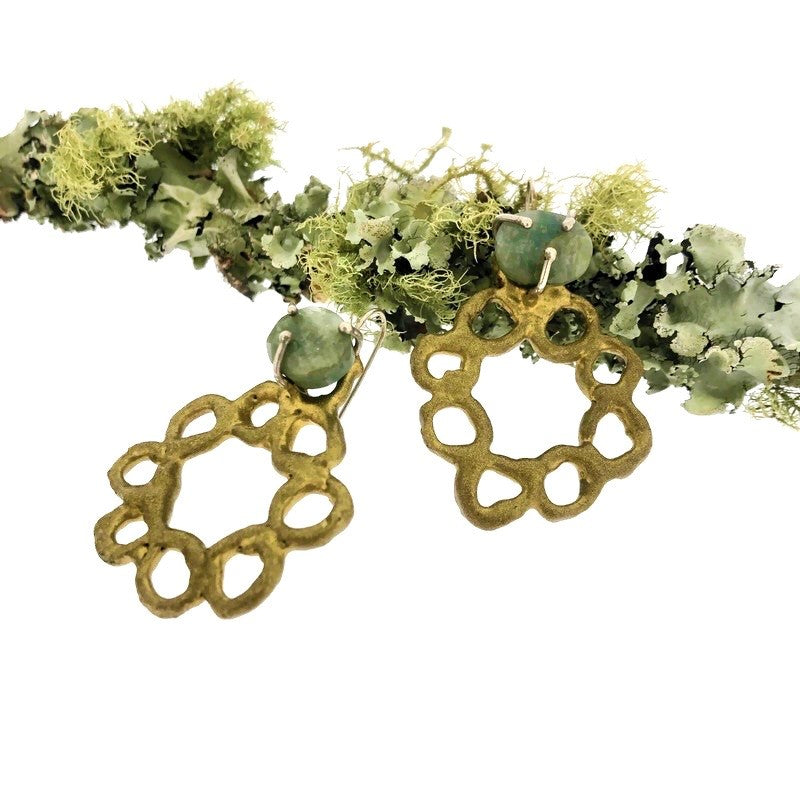 Full view of Emerald Wreath Earrings on branch. These earrings resemble the shape of a wreath made of metal that has a bronze powdercoat. Set at the top of the wreath is an opaque emerald.