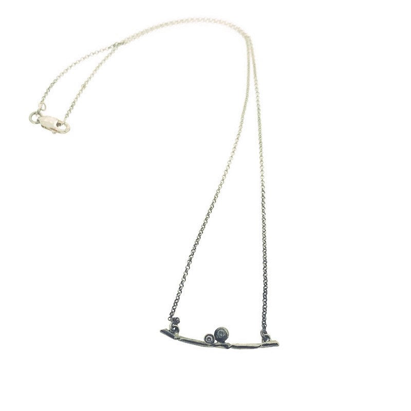 Full view of Essa Necklace. This necklace is made of sterling silver and has a bar pendant in the shape of a silver branch that has two set diamond coming out of the top.
