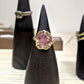 Full view of Roxanna Ring - Large on black pedestal. The Roxanna features organic carved metalwork with a delicately dappled surface.     A large 1.4 asymmetrical shaped Umba Sapphire in a beautiful shade of pale pink is set in 14K (recycled) Yellow Gold. 